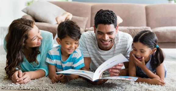 Family laying on their stomachs on the floor reading a book